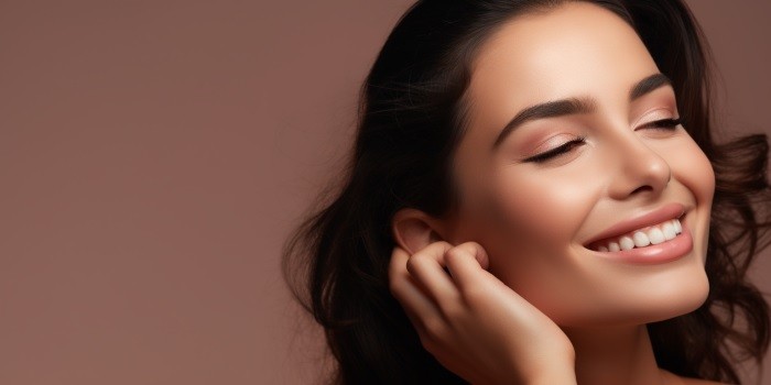 A young girl with dark hair smiles and touches her face