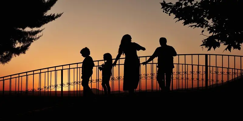 Silhouette of a family of four walking across a bridge during a sunset