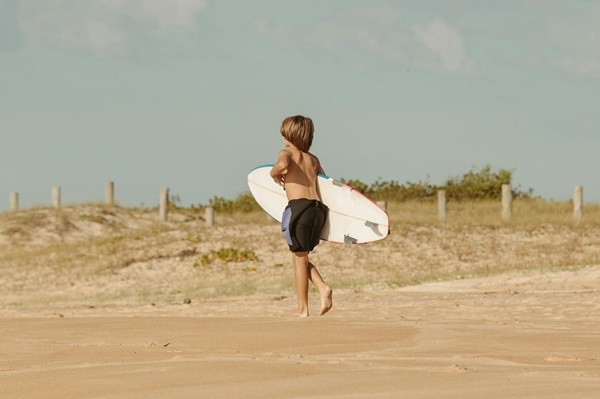 Boy carrying a surfing board on a beach in Miami to represent reasons to move to Miami with your toddler