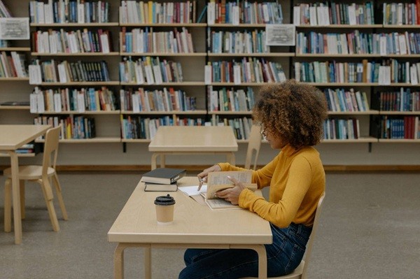 College in Yellow Long Sleeve Shirt Sitting on Chair in library reading book