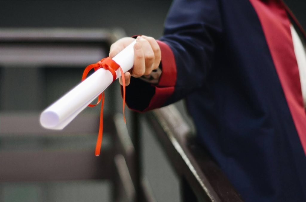 person wearing graduation gown holding out diploma